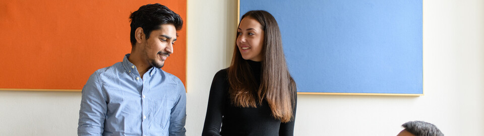 Drei Auslandsstudierende befinden sich mit einem Globus in einem Seminarraum. Eine Studentin zeigt auf ein Land auf dem Globus.