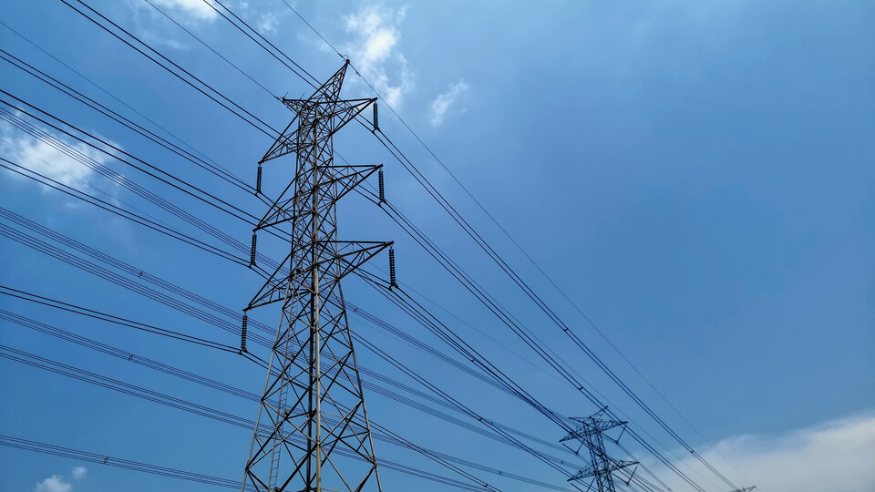 Zwei Strommasten mit gespannten Stromkabeln vor blauem Himmel